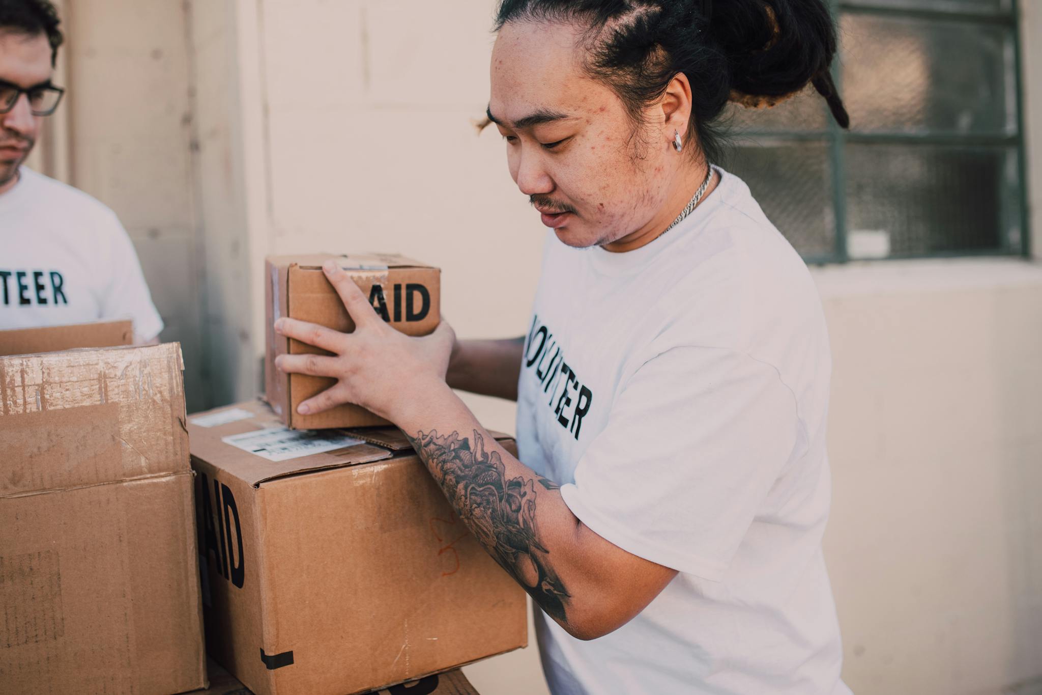 Asian male volunteer handling aid boxes during charity event indoors.